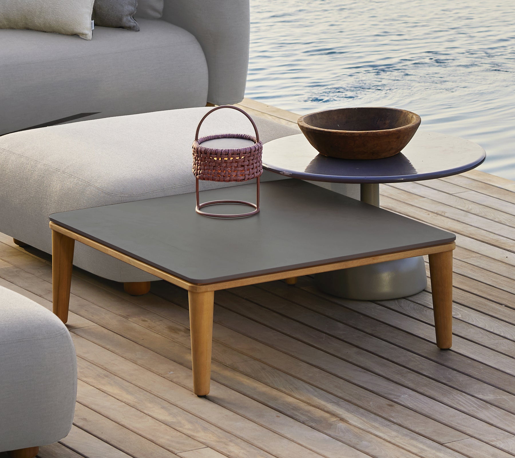 Modern grey table with a wooden bowl and a metal basket in an outdoor setting.