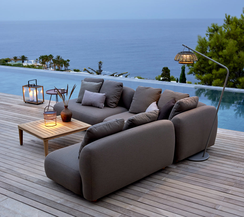 Grey sofa with wooden table and lanterns by a poolside overlooking the ocean.