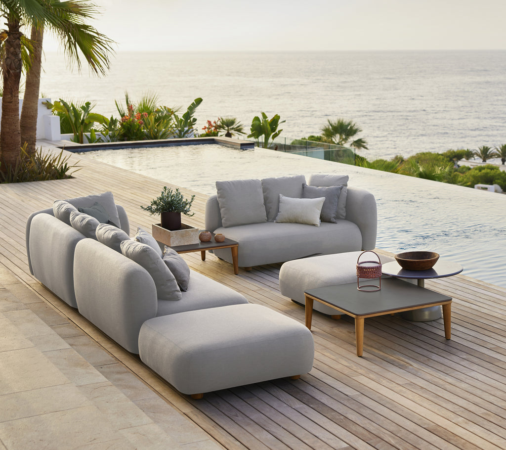 Stylish grey sofa with cushions and a black coffee table in a modern outdoor lounge by the sea.