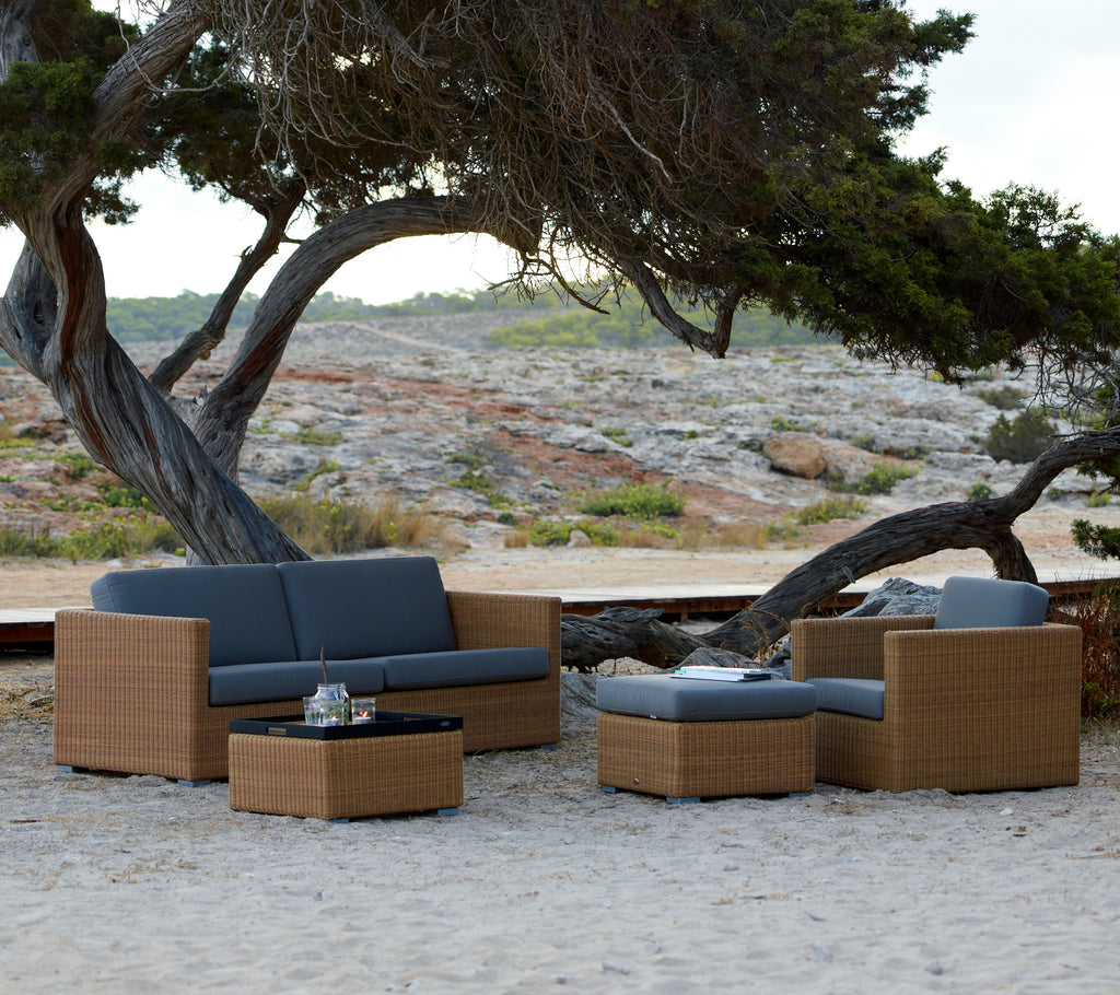 Modern brown lounge furniture with grey cushions set in a natural outdoor environment.