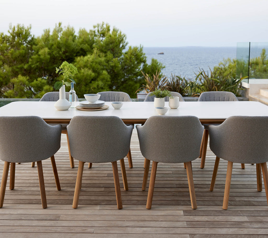 A modern table set with gray upholstered chairs, surrounded by greenery and a serene ocean view, perfect for dining and gatherings.