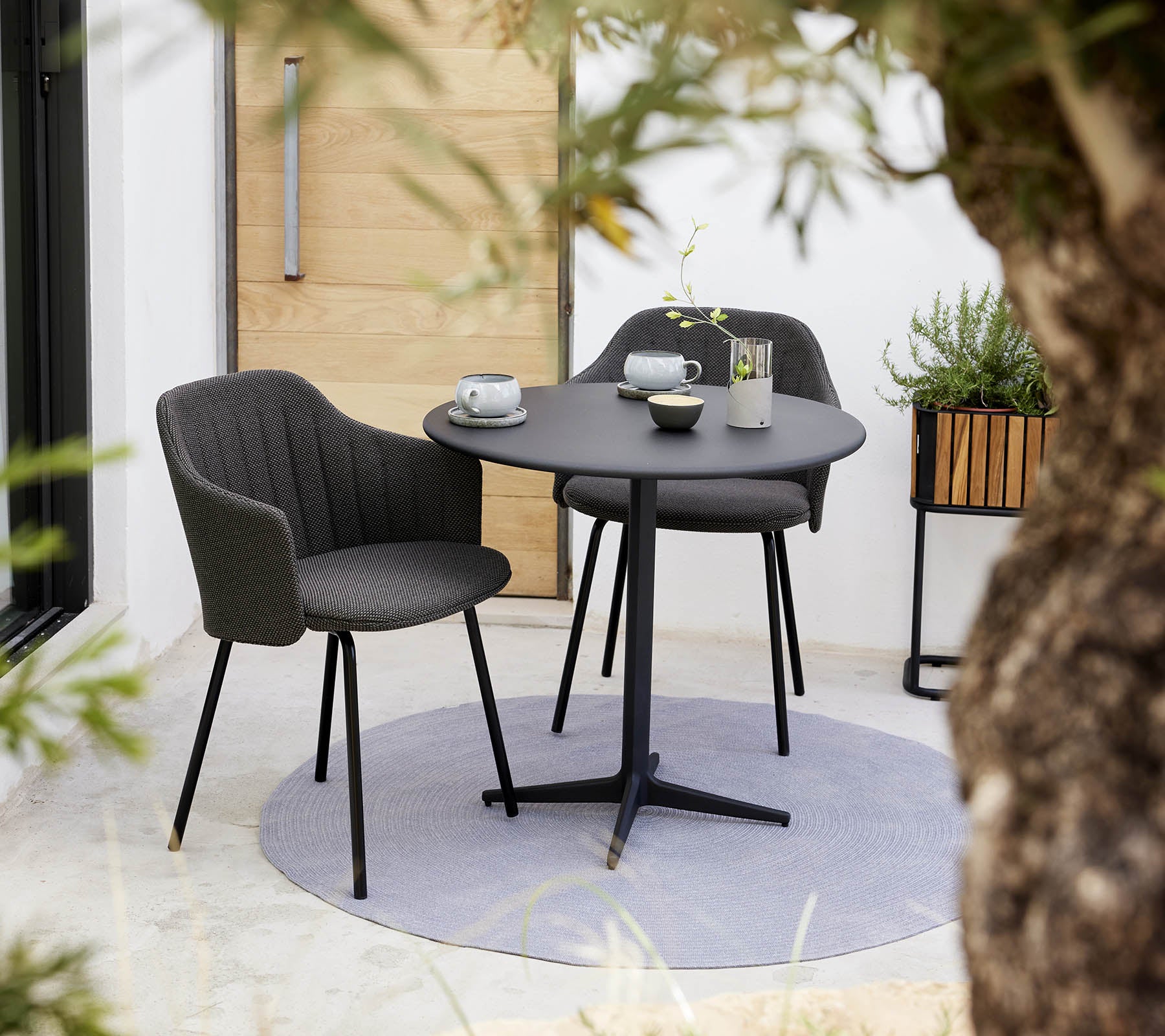 Stylish choice chair and round drop café table set, accompanied by a cup and saucer, surrounded by greenery.