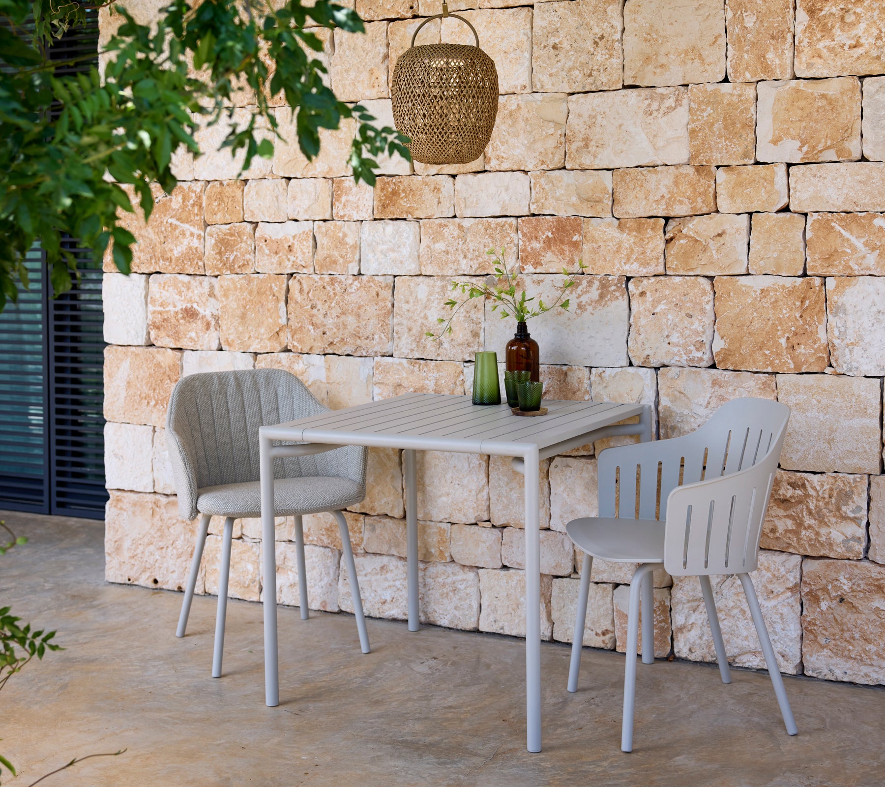 Modern grey table and chairs with green and brown bottles in an outdoor setting.