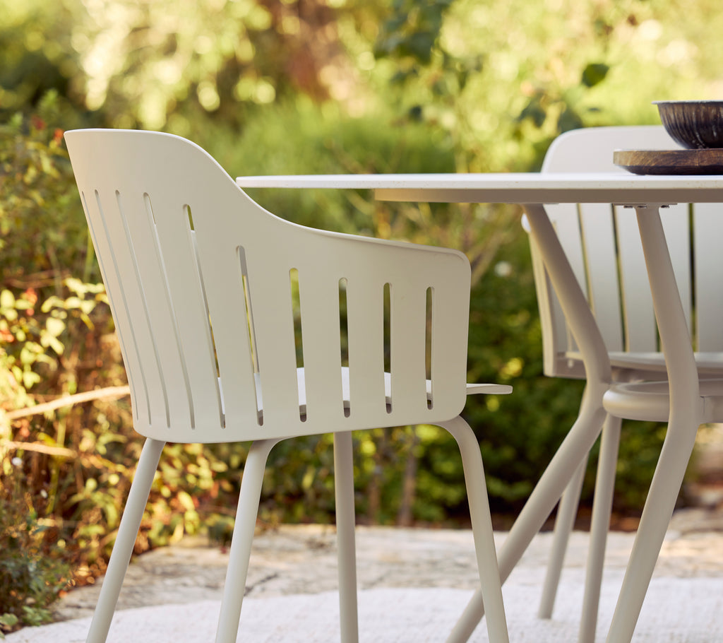 Modern white chair beside a table in an outdoor setting surrounded by greenery.
