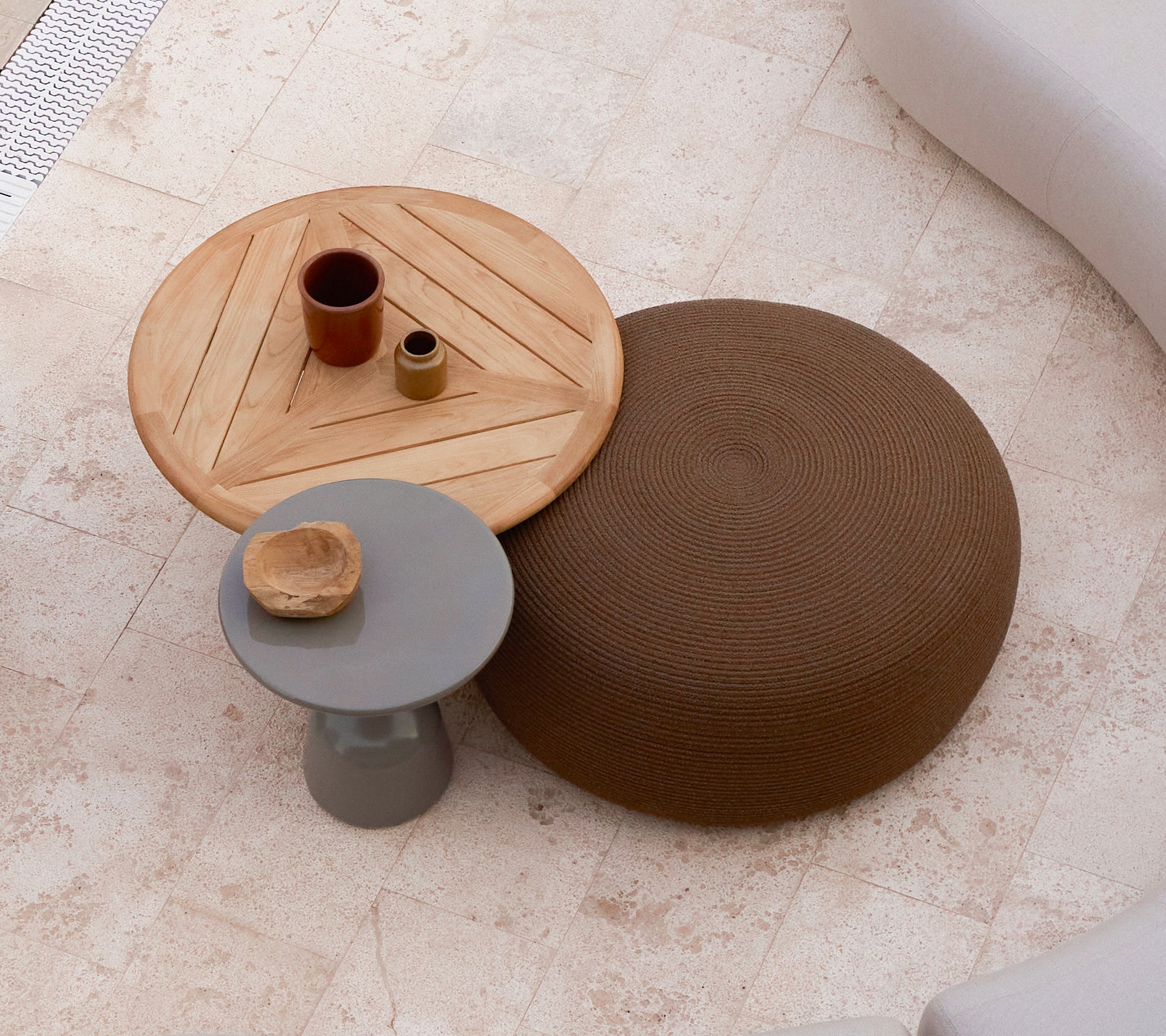 A large circular footstool in brown next to a wooden coffee table with a geometric design, featuring small decorative items on top.