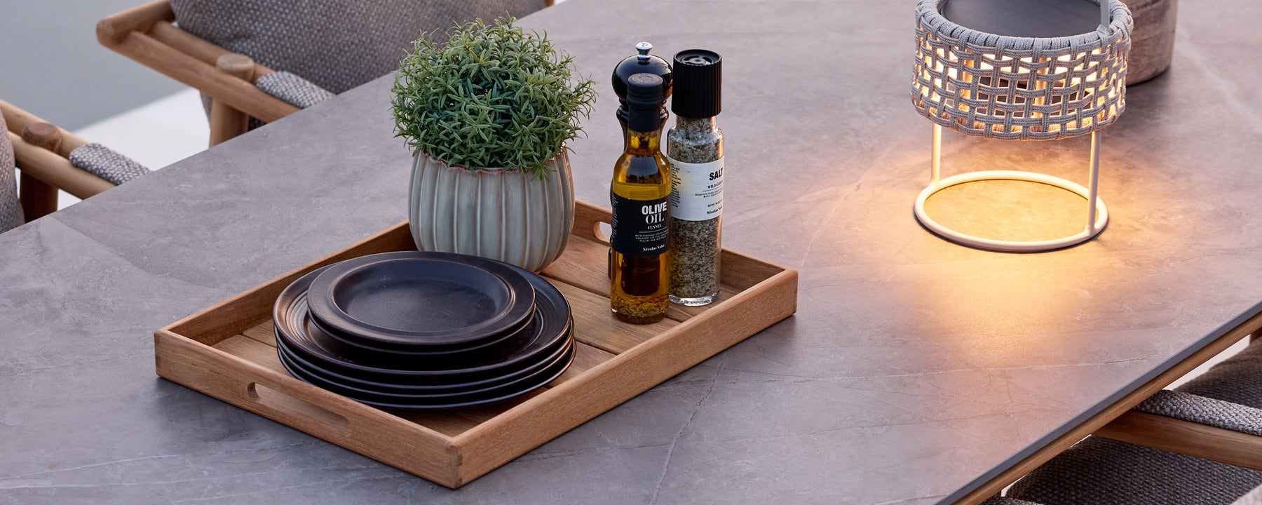 Black plates, olive oil bottle, and small plant arranged on a tray on a dining table.