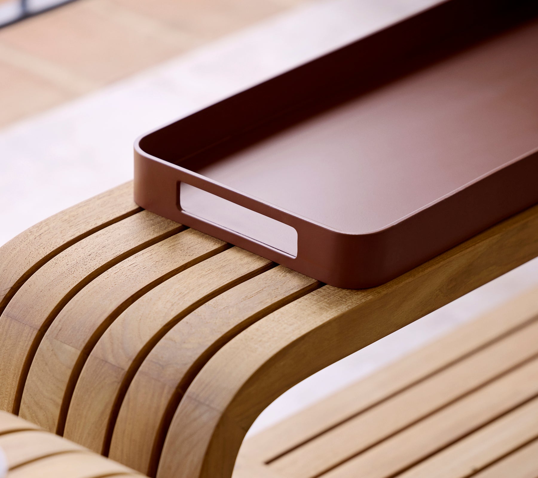 Close-up of a sleek desert red club tray resting on a smooth, curved wooden surface, highlighting its minimalist design.