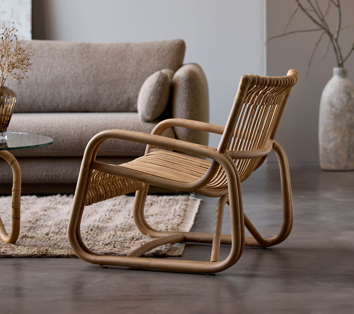 Rattan chair beside a beige sofa and glass table in a modern lounge setting.