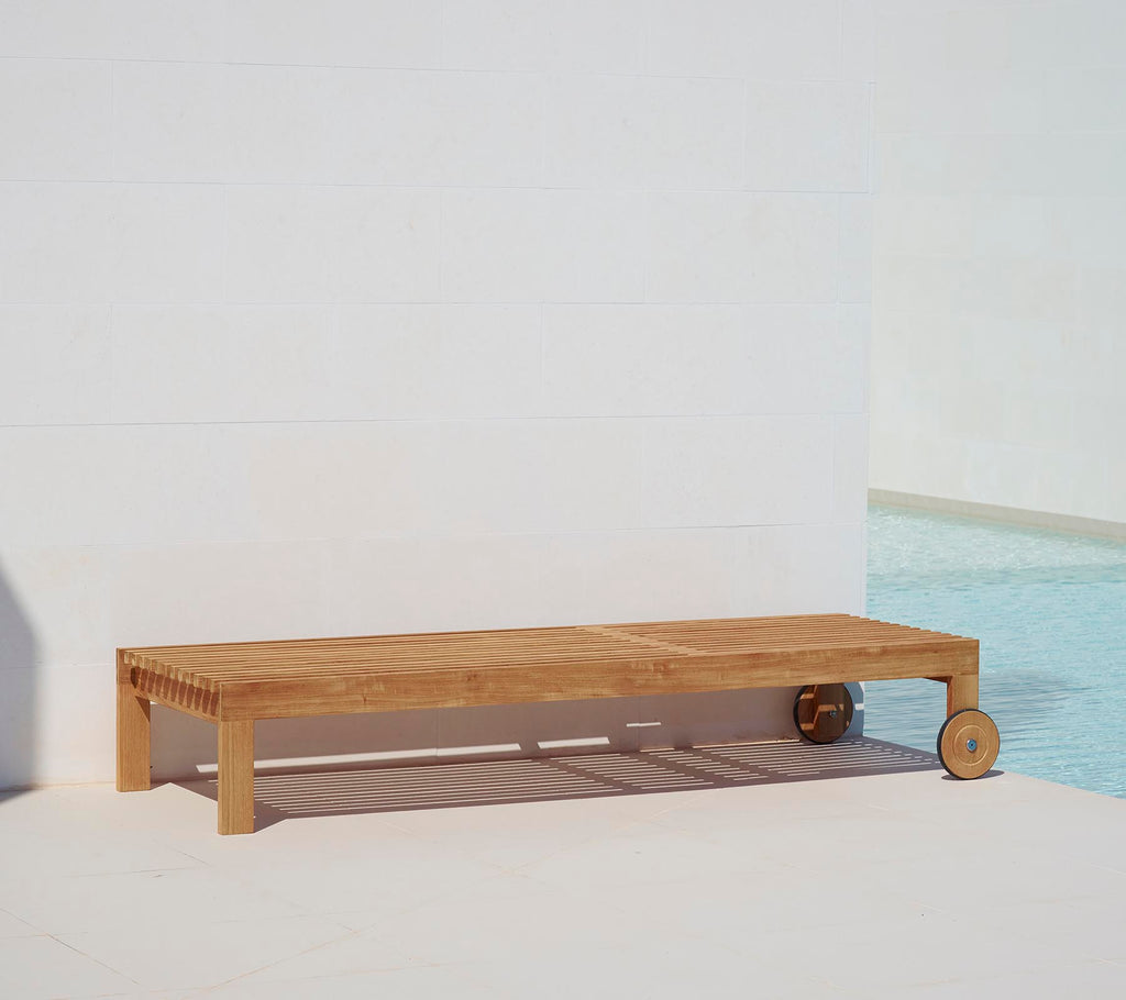 Wooden sunbed with a minimalist design, featuring a sleek surface and a wheel for easy mobility. Ideal for relaxation by the pool.