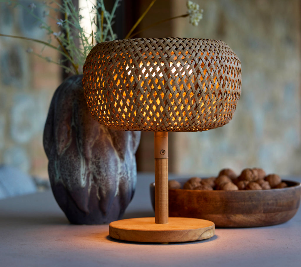 Small woven lamp with a warm glow, complemented by a decorative vase and a bowl of nuts, creating a cozy atmosphere.