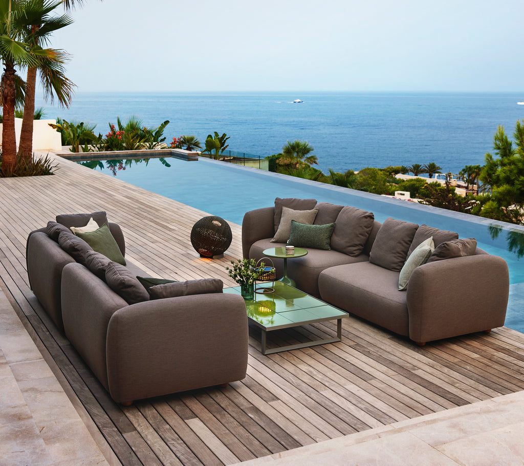 Stylish lounge seating featuring soft gray cushions, a glass coffee table, and a serene ocean view. Ideal for relaxation.