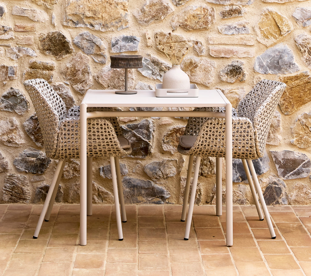 A small dark grey illusion lamp on a Bliss table with two Vibe chairs, surrounded by a textured stone wall.