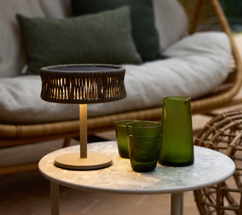 A small dark grey illusion lamp on a marble coffee table, accompanied by green decorative glass vases and a cozy seating area.