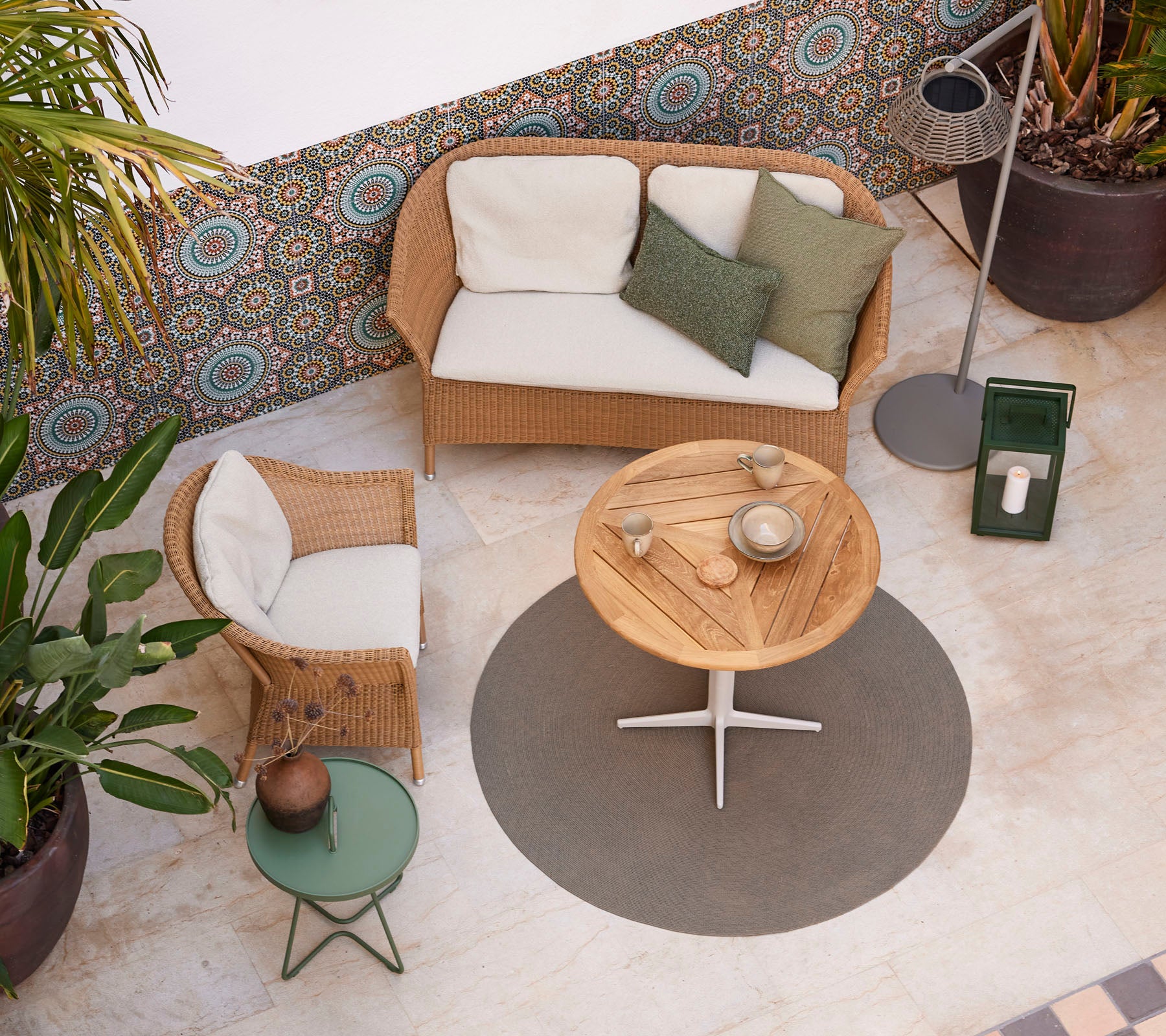 A cozy seating arrangement featuring a rattan sofa, a round wooden coffee table, and potted plants, enhancing a stylish atmosphere.