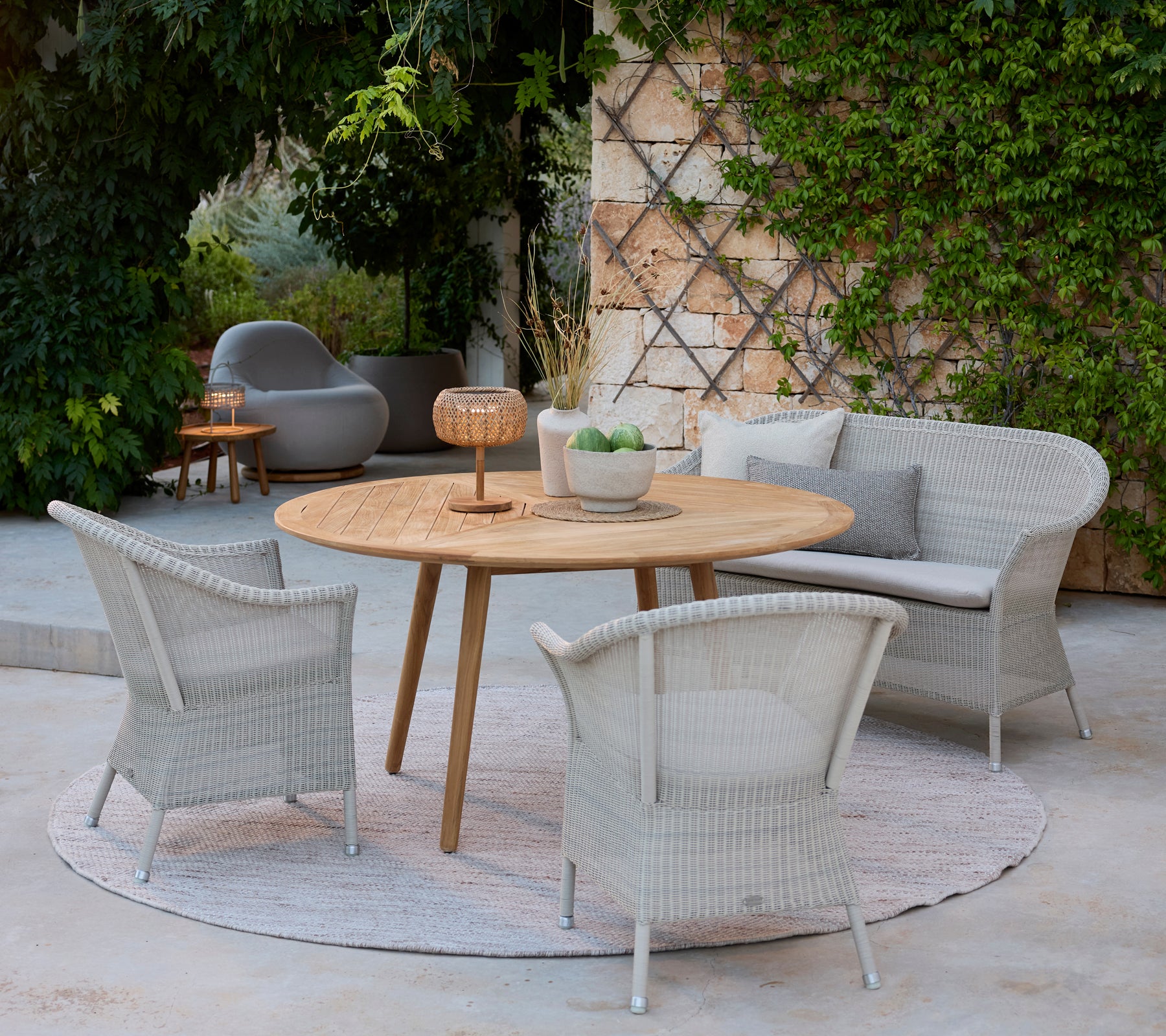 Modern lounge area featuring grey chairs, a round wooden table, and a grey sofa surrounded by greenery.
