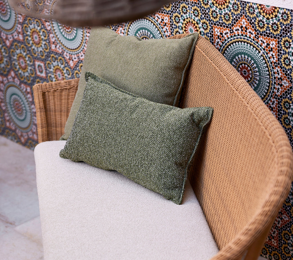 Two green scatter cushions on a light-colored sofa, positioned against a vibrant, patterned backdrop featuring circular designs.