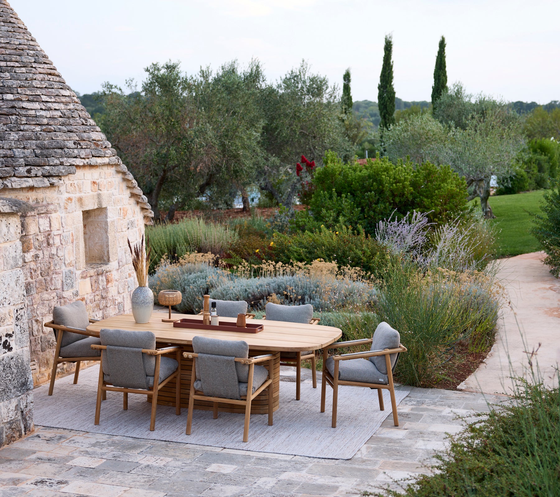 Modern outdoor dining setup with a round table and grey chairs surrounded by greenery.