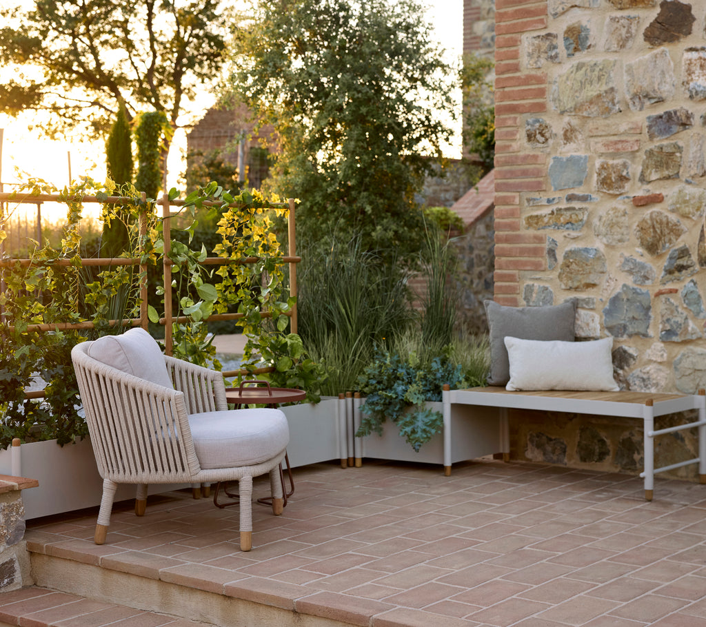 Moments lounge chair beside a Sticks planter and Sticks planter bench, set against a stone wall in a serene outdoor space.