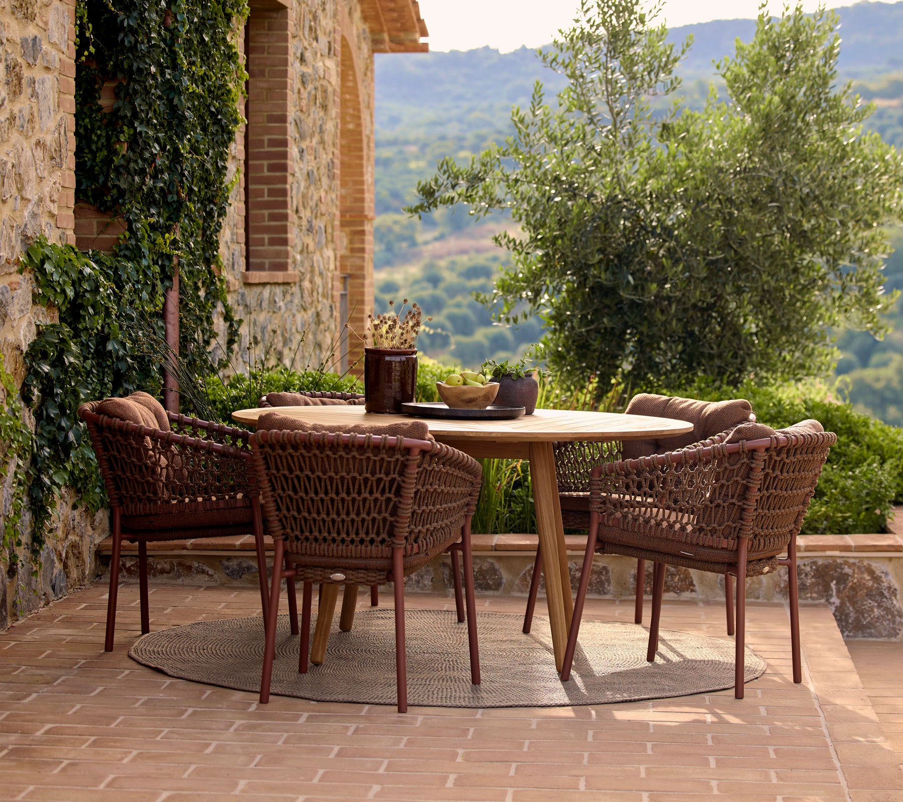 A round dining table surrounded by four umber brown Ocean dining chairs, set against a lush outdoor backdrop.