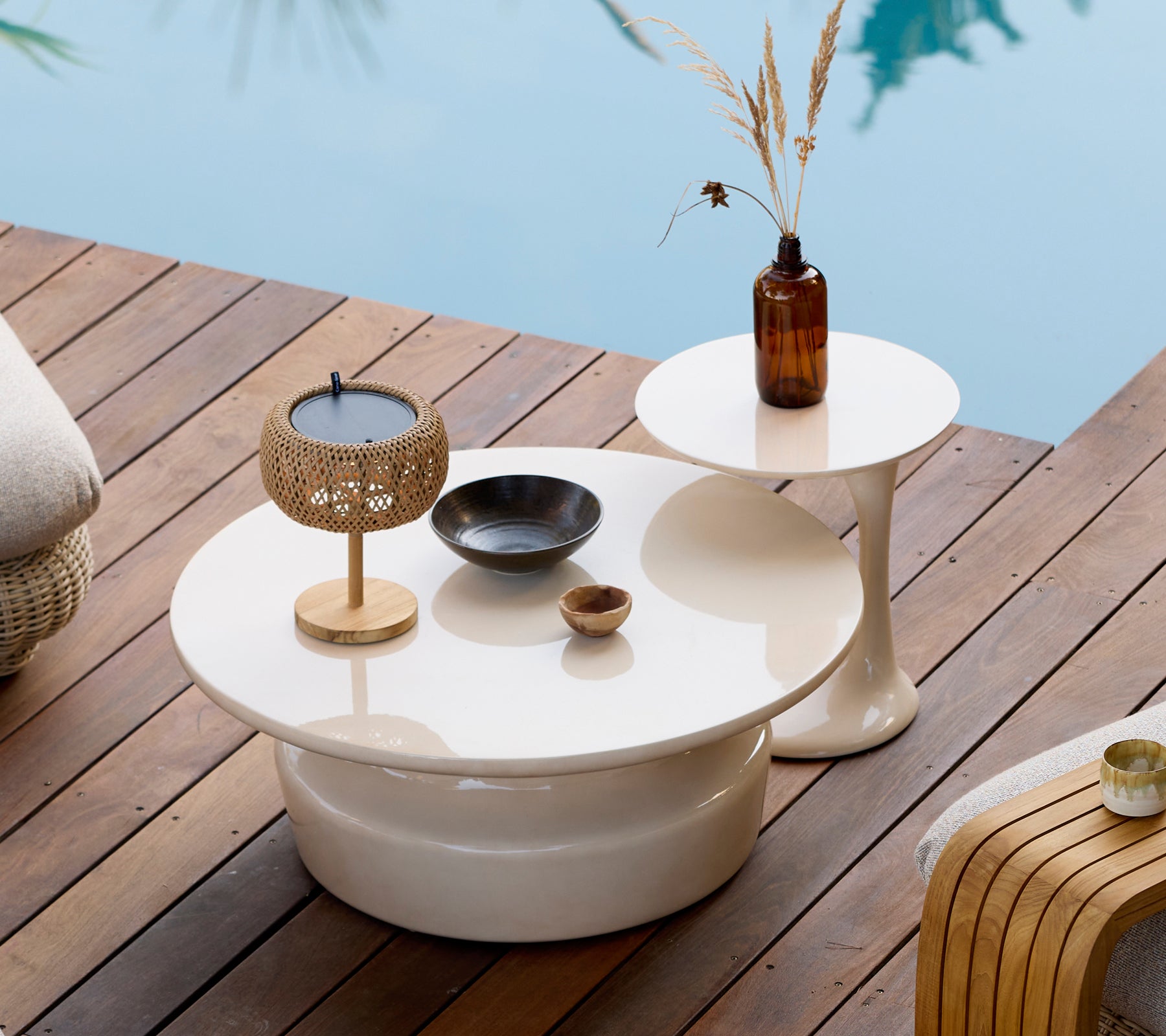 Modern outdoor setting with white coffee and side tables, gold candle holder, and brown vase.
