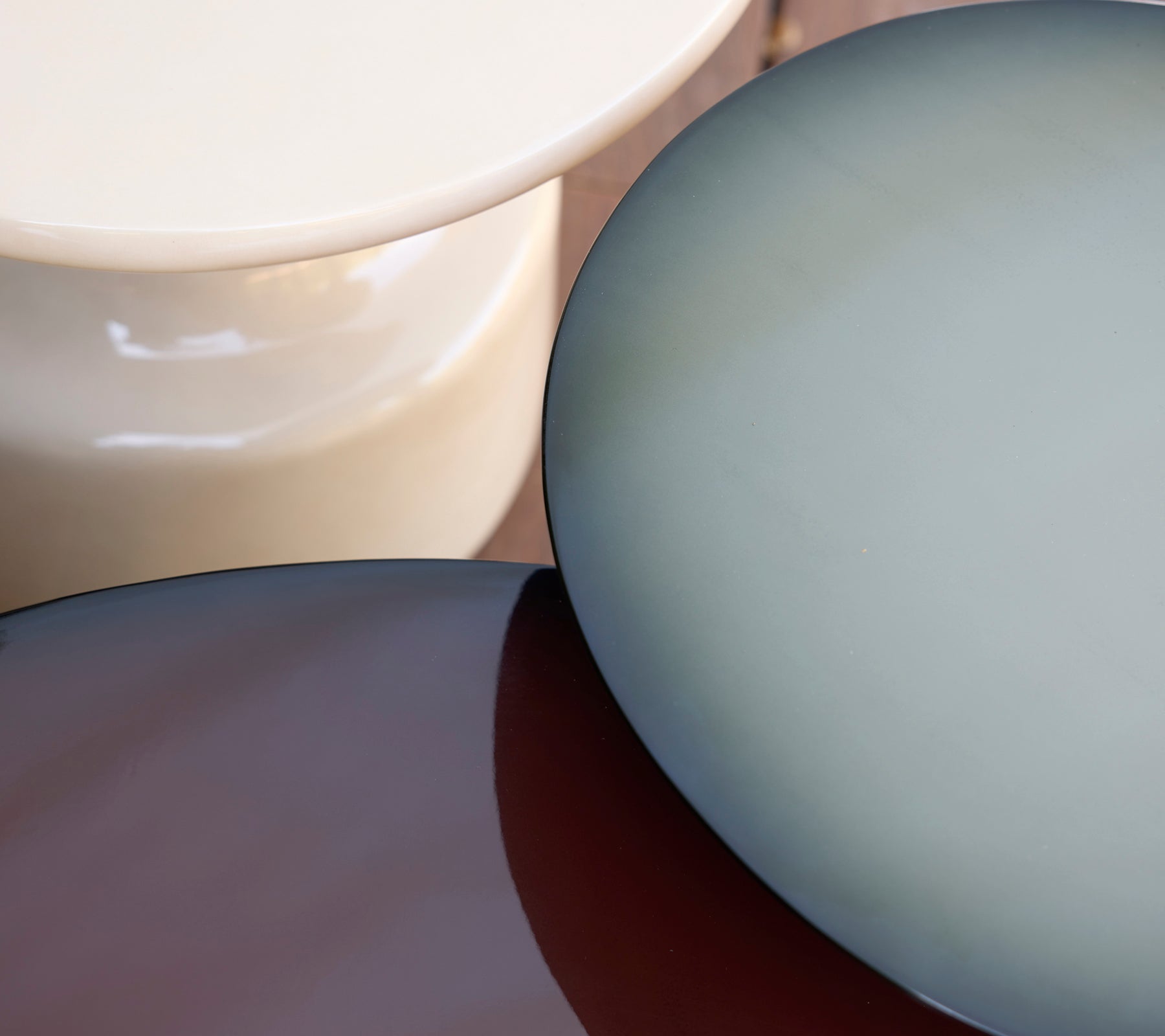 Three modern tables in cream, blue, and brown hues arranged together.