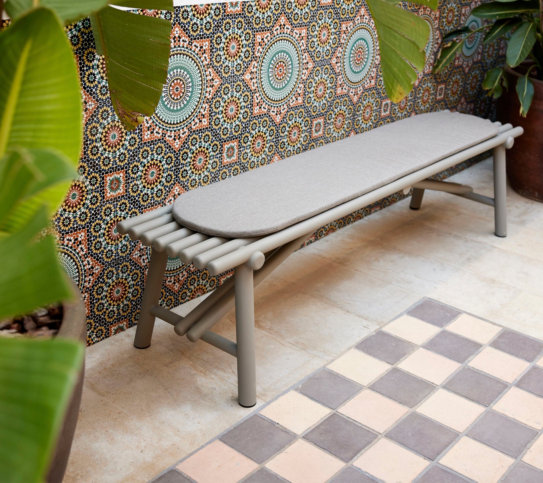A sleek bench featuring stick-like design elements, complemented by a geometric patterned backdrop and vibrant greenery.
