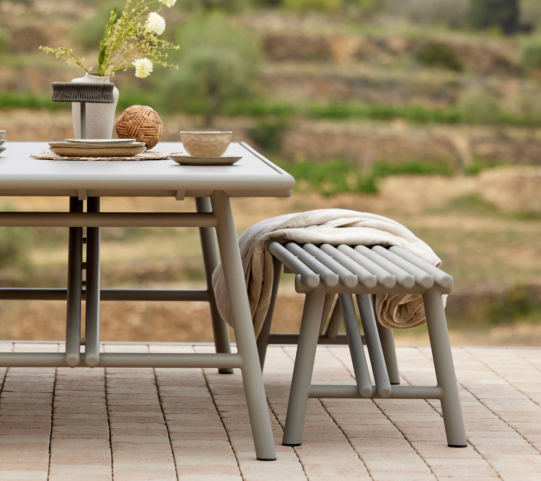 A stylish table setting with bowls, cups, and a decorative centerpiece, accompanied by a matching stick-style stool.
