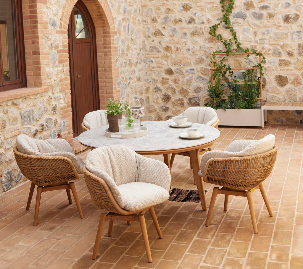 A stylish seating area featuring rounded chairs and a circular table, complemented by greenery in a planter against a stone wall.