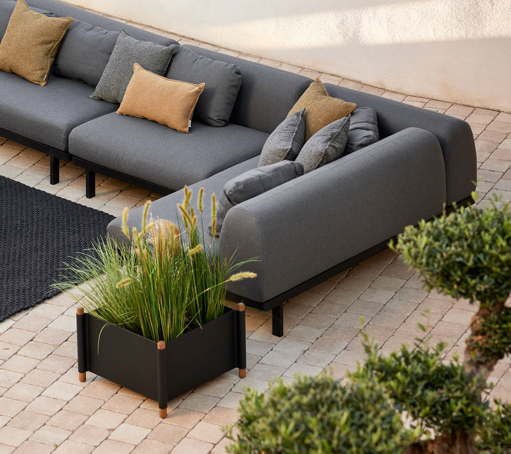 Lava gray sofa with decorative pillows alongside a modern sticks planter filled with lush greenery, set on a textured surface.