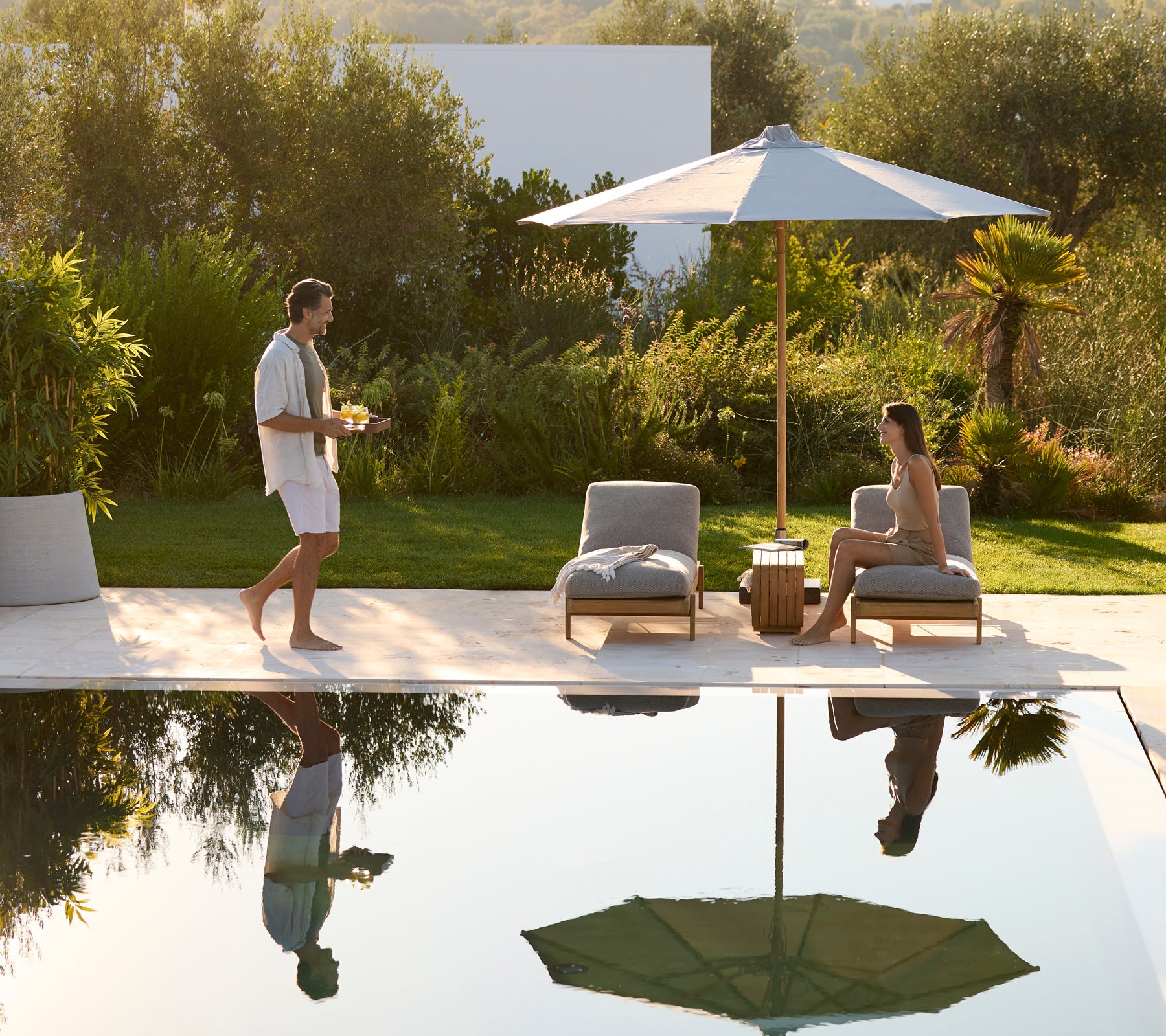 Two Vista sunbeds with guests relaxing by the pool under an umbrella