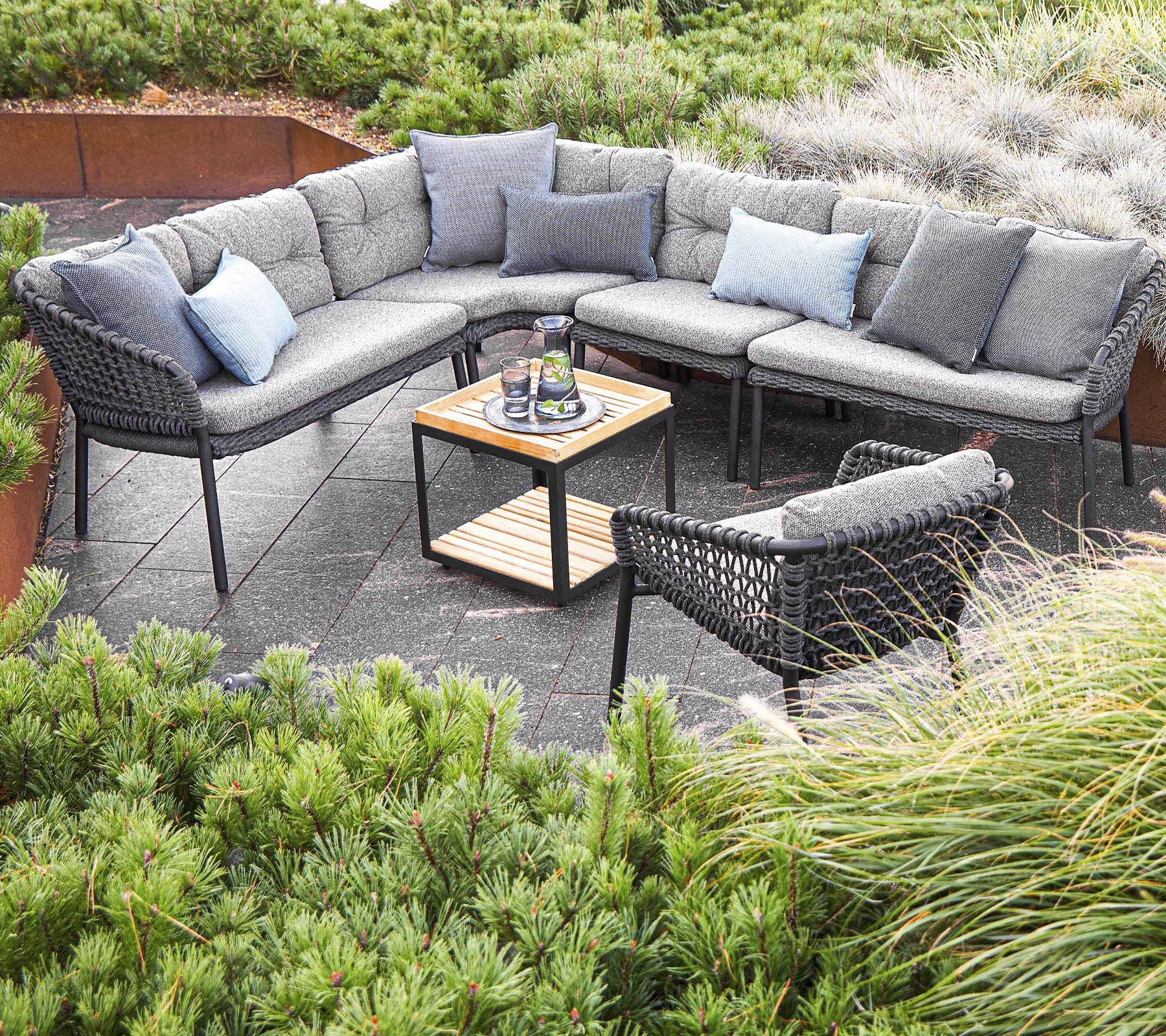 Stylish outdoor seating arrangement featuring a sectional sofa with cushions and a central table, surrounded by greenery.